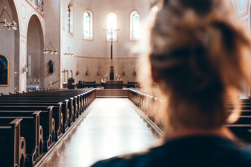 Woman viewed from behind, looks down center aisle of church.